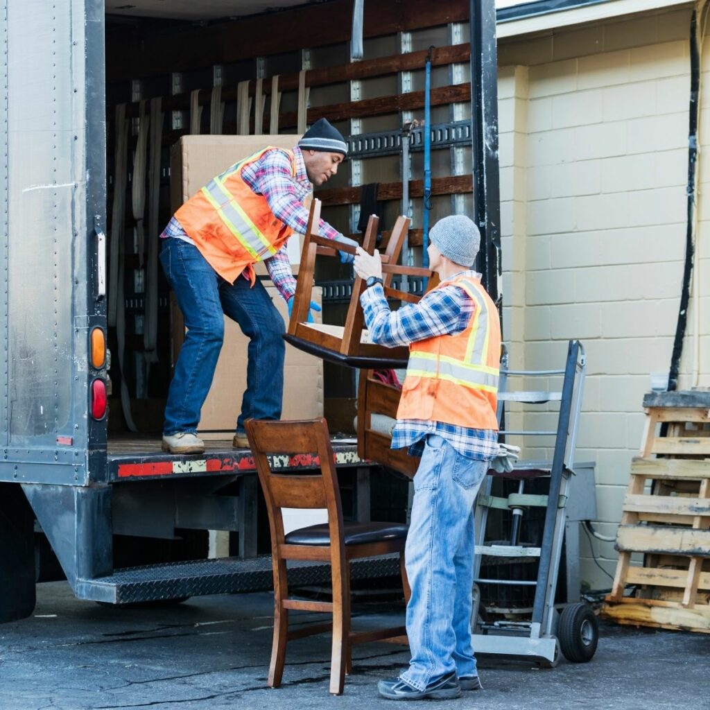 Two employees loading furniture into a dump the junk truck