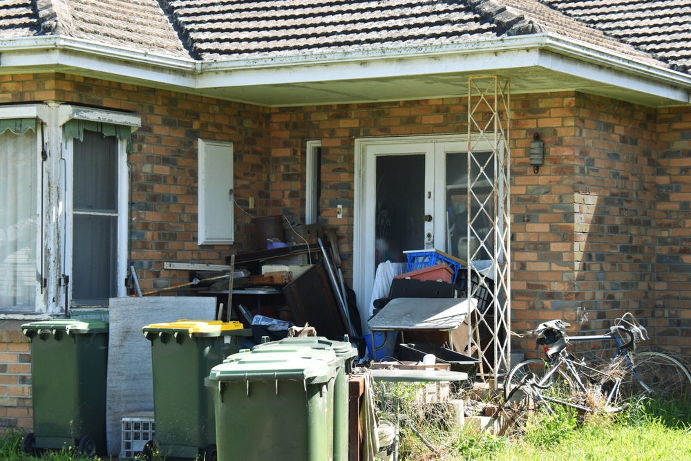 An old brick house with abandoned junk in the front yard.